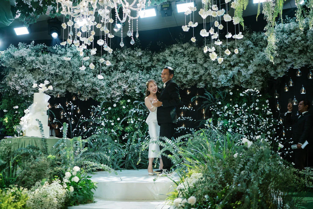 Amidst a backdrop of soft white florals and flickering candlelight the bride and her father on the dance floor