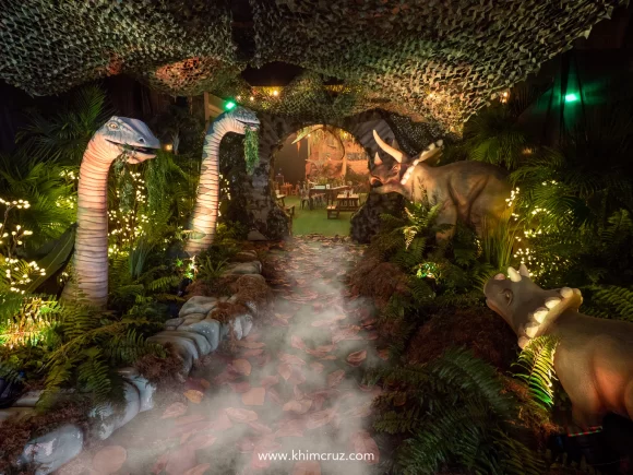 Brachiosaurus emerging from a lake and Triceratops roaming the forest at the entrance of dinosaur-themed birthday