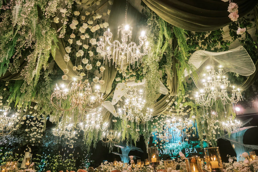 Green and white hues mingle seamlessly at the wedding reception, accentuated by airy floral chandeliers and the gentle glow of candles