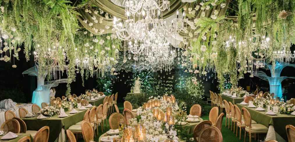 a harmony of lush greens and soft whites sets the tone complemented by elegant floral chandeliers and glowing candles at the wedding reception