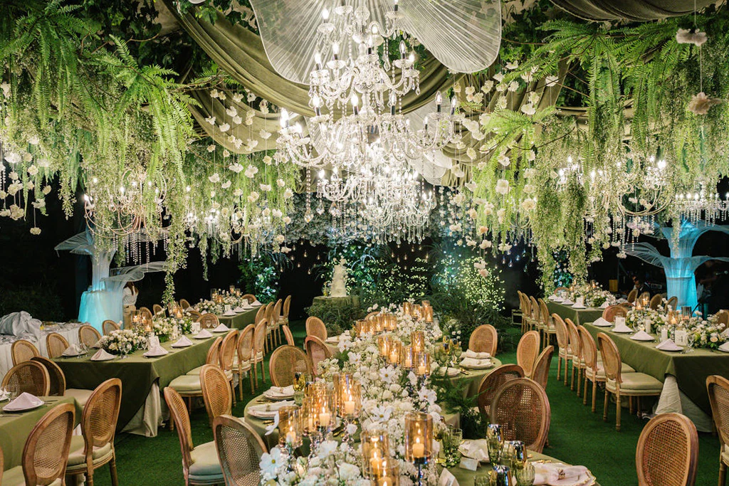 a harmony of lush greens and soft whites sets the tone complemented by elegant floral chandeliers and glowing candles at the wedding reception