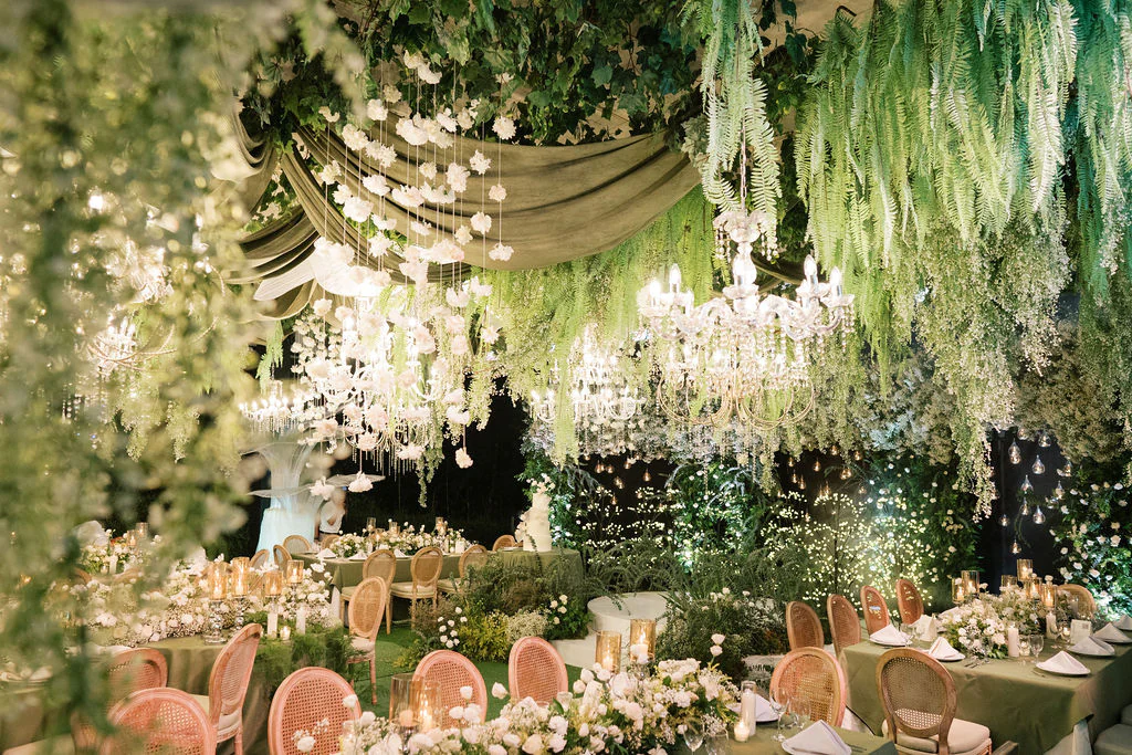 harmony of lush greens and soft whites sets the tone complemented by elegant floral chandeliers and glowing candles at the wedding reception