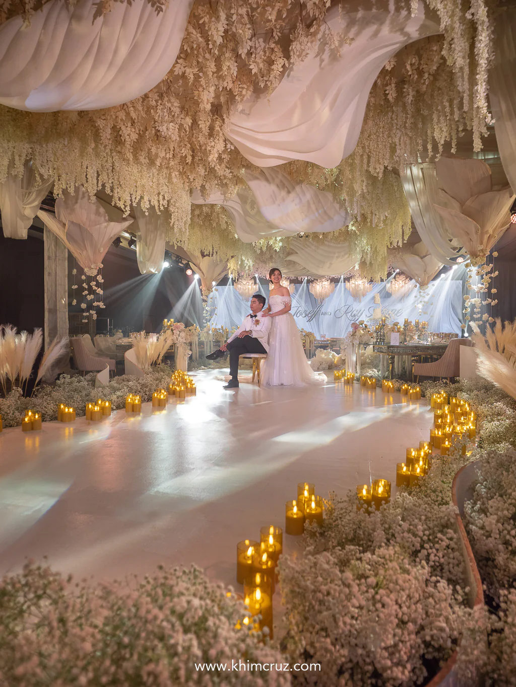 couple surrounded with candles with hanging floral arrangements