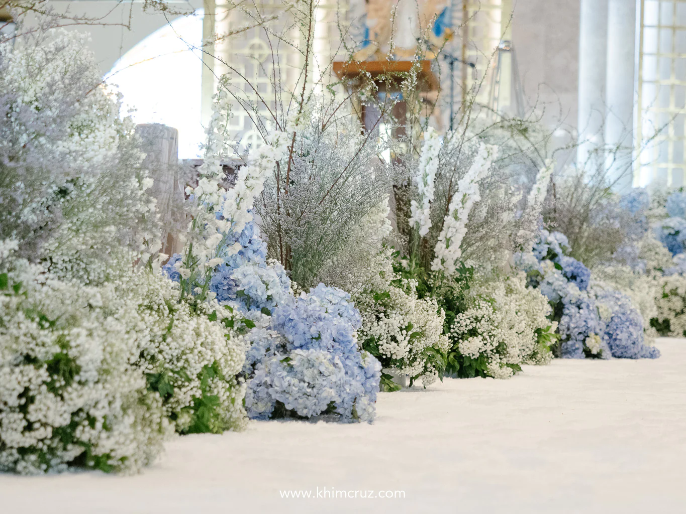 white and blue color featuring hydrangeas babys breath floral arrangements stand tall on both sides of wedding ceremony