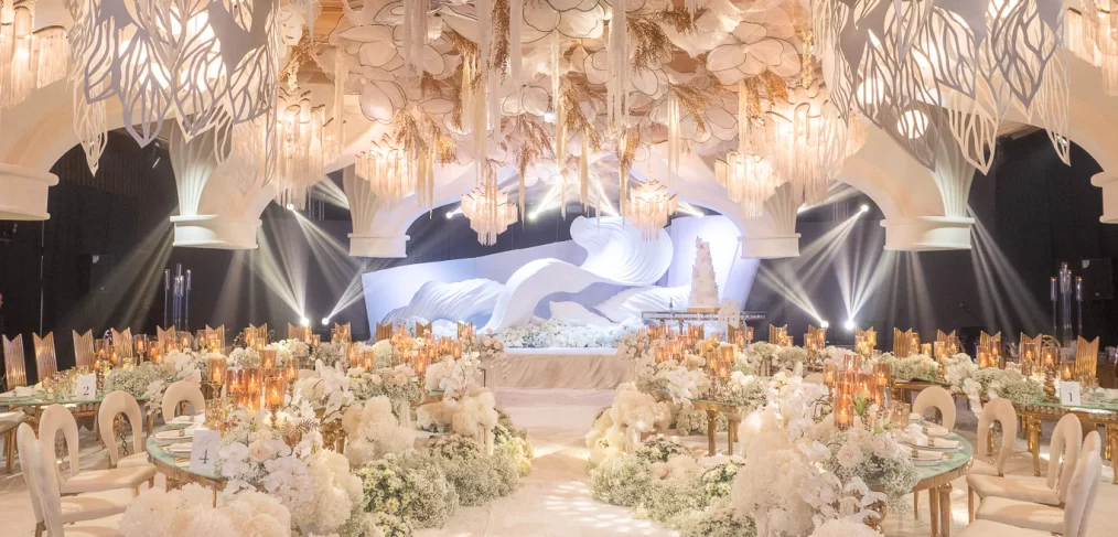 a wave-like backdrop sets the stage with suspended florals and arching ceiling structures add depth and elegance to this wedding reception