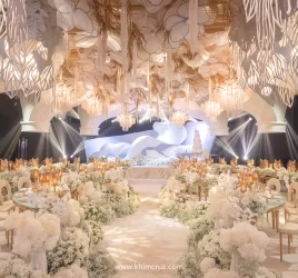 a wave-like backdrop sets the stage with suspended florals and arching ceiling structures add depth and elegance to this wedding reception