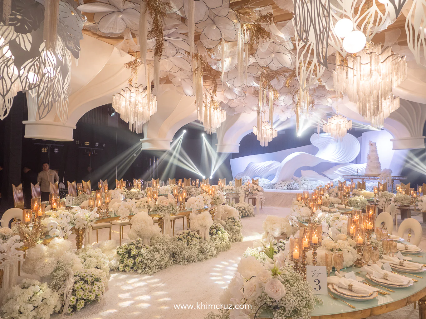 ceiling treatment features suspended floral installations and arching structures bringing depth to this ethereal wedding reception