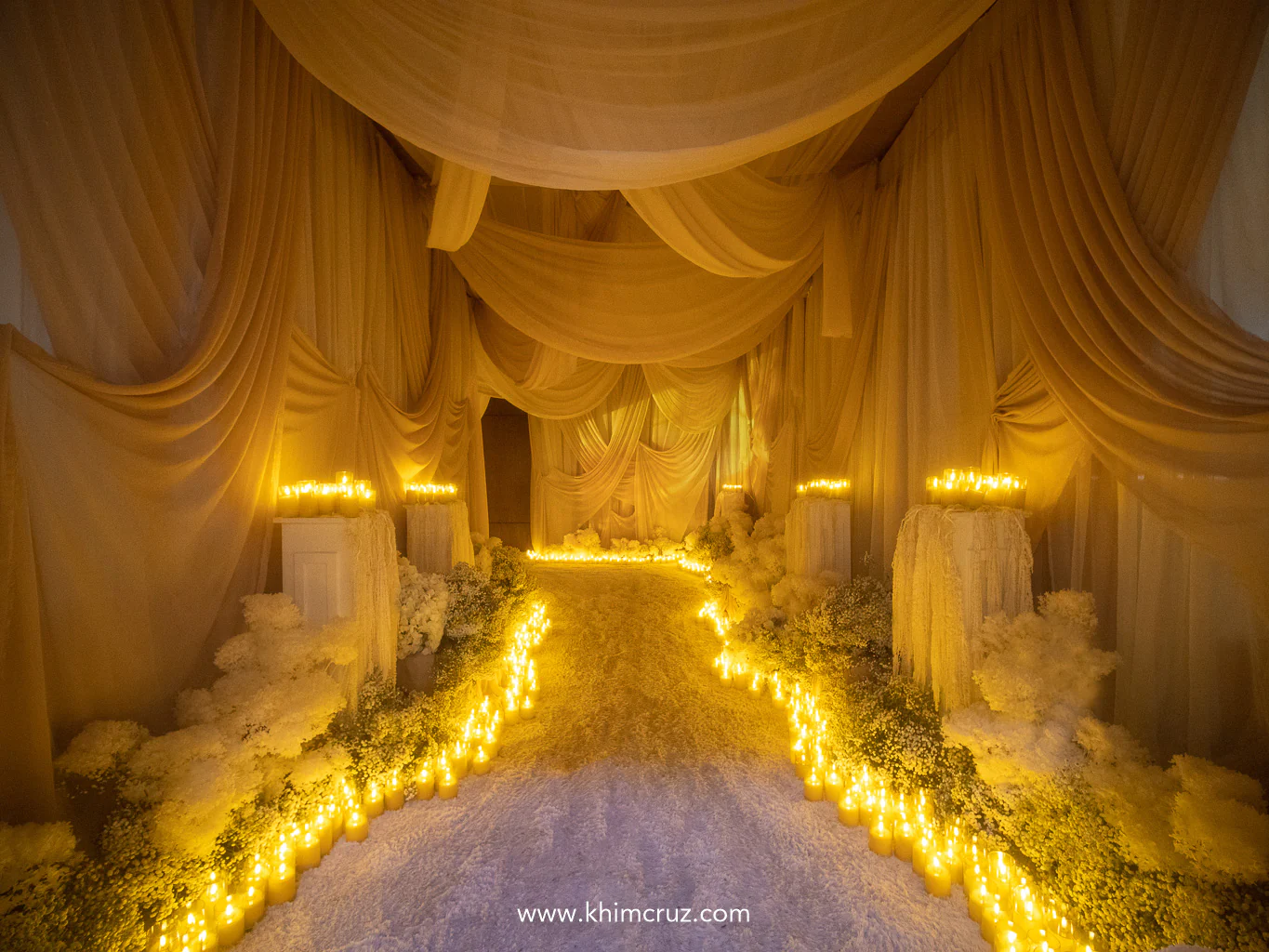 wedding entrance tunnel is adorned with continuous white florals and warm glow of candles